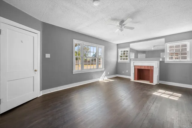 an empty room with wooden floor fireplace and windows