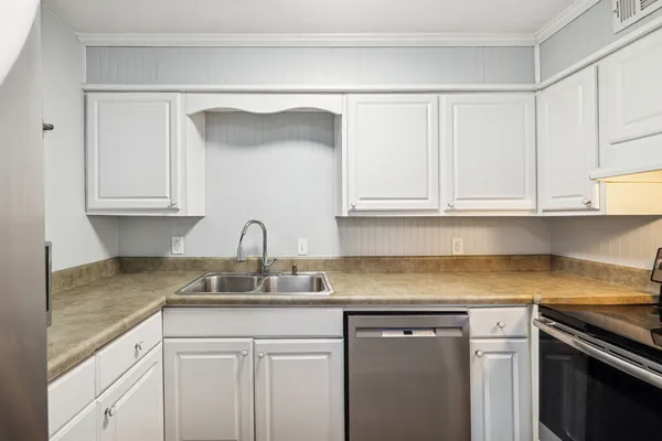 a kitchen with stainless steel appliances granite countertop a sink dishwasher a stove and white cabinets with wooden floor