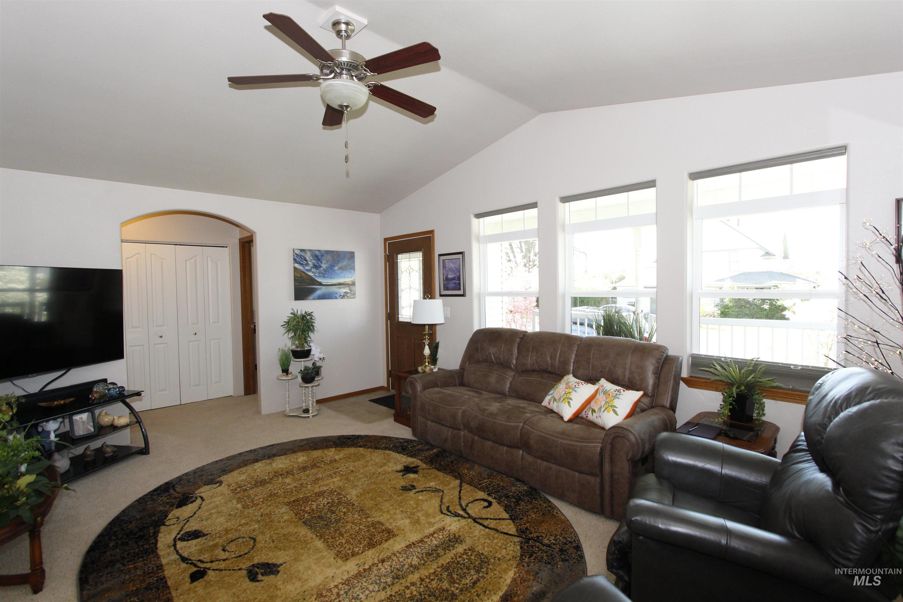 1803 16th Street Lewiston, ID 83501 - Photo 5 of 22 Vaulted ceiling living area featuring a ceiling fan with integrated lighting, three large windows, an arched doorway, and bi-fold closet doors