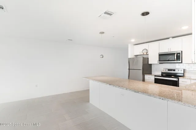 a kitchen with granite countertop stainless steel appliances a refrigerator a stove top oven and sink