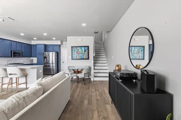 a living room with stainless steel appliances furniture a clock and a view of kitchen