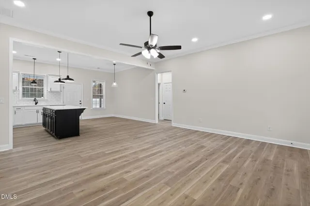 a view of an empty room with chandelier fan and kitchen view