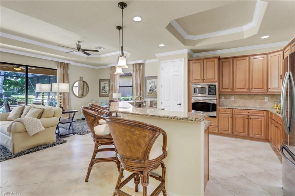 9434 Piacere Way Naples, FL 34113 - Photo 32 of 32 Kitchen with stainless steel appliances, a raised ceiling, crown molding, open floor plan, and light stone counters