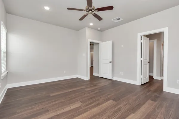 an empty room with wooden floor ceiling fan and windows