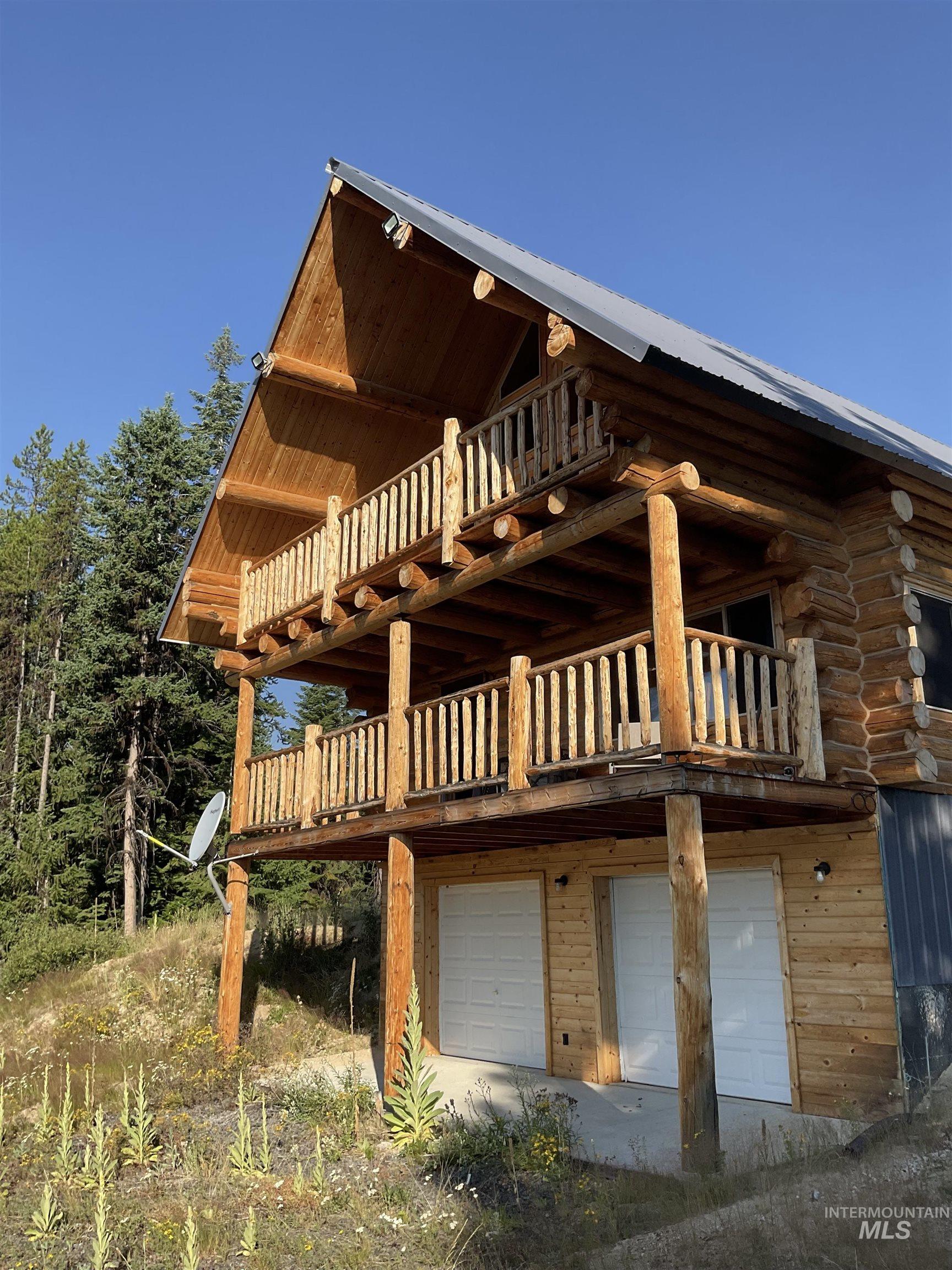 625 Rhett Creek Road Elk City, ID 83525 - Photo 11 of 48 Log cabin style exterior with a metal roof, featuring a two-story balcony with log railings, and two garage doors on the lower level