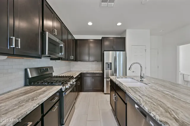 a kitchen with stainless steel appliances kitchen island granite countertop a refrigerator a sink dishwasher and a stove with wooden floor