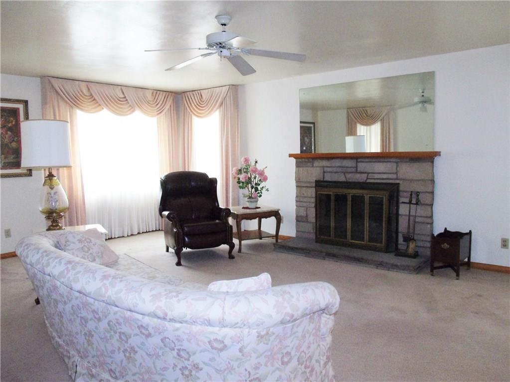 2103 Ridge Road Jeannette, PA 15644 - Photo 3 of 19 Huge formal livingroom with several windows, stone log burning fireplace, plaster walls and hardwood flooring under carpeting, fan and neutral dcor.