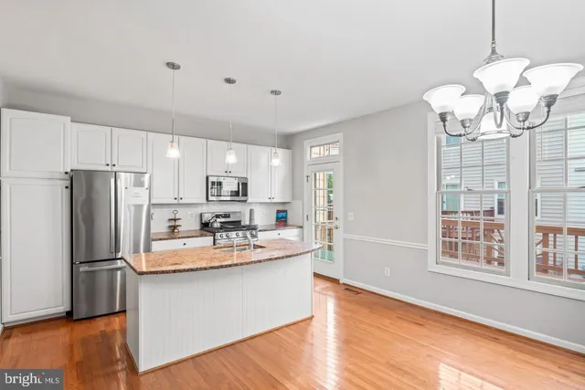 a kitchen with stainless steel appliances granite countertop a refrigerator a sink dishwasher a stove and white cabinets with wooden floor