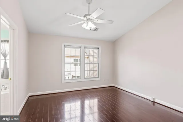 an empty room with wooden floor chandelier fan and windows