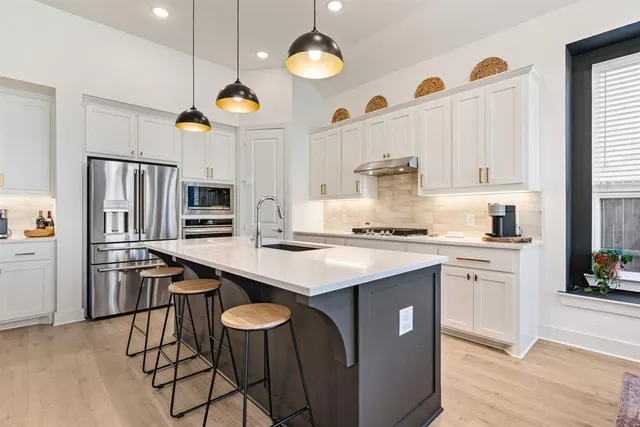 a kitchen with stainless steel appliances granite countertop a sink a stove a refrigerator and island with wooden floor