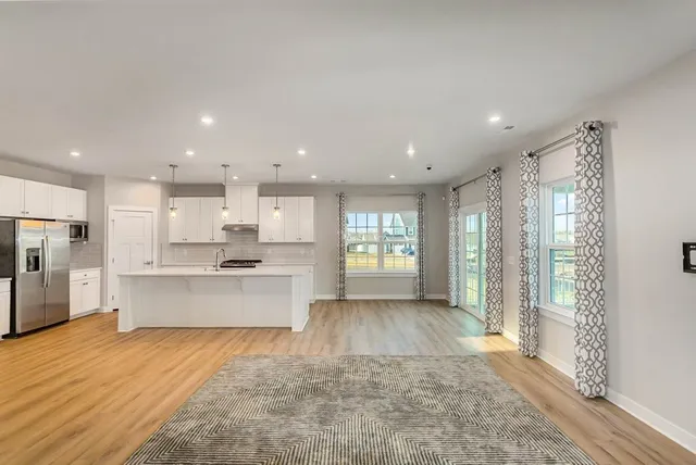 a large kitchen with stainless steel appliances kitchen island a large counter top a stove a refrigerator with white cabinets and wooden floor