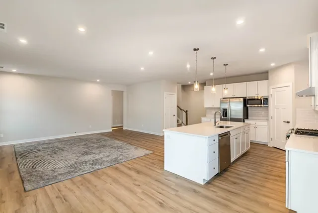 a large kitchen with a stove a sink a refrigerator and white cabinets with wooden floor