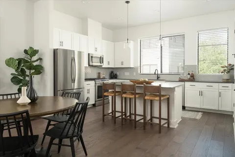 a kitchen with stainless steel appliances a dining table chairs refrigerator and sink
