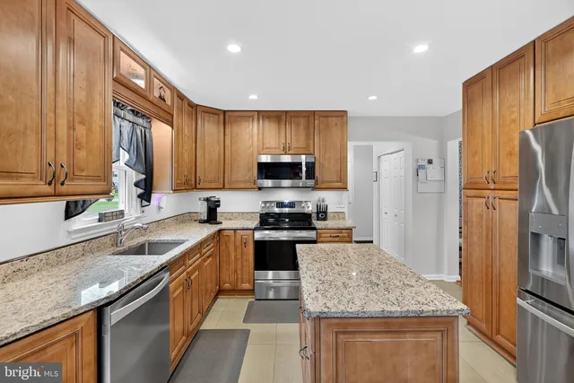 a kitchen with stainless steel appliances granite countertop a sink stove refrigerator granite counter tops wooden cabinets and wooden floor