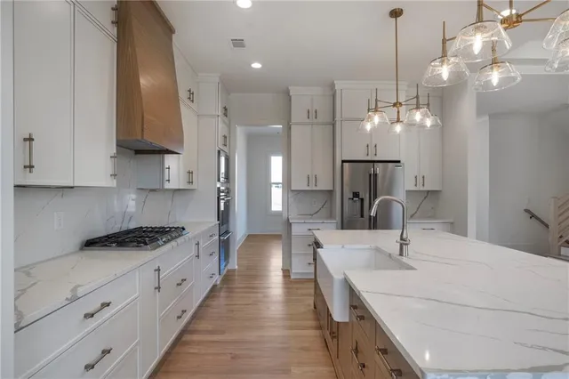 a large kitchen with stainless steel appliances a large counter top a stove a refrigerator and a chandelier