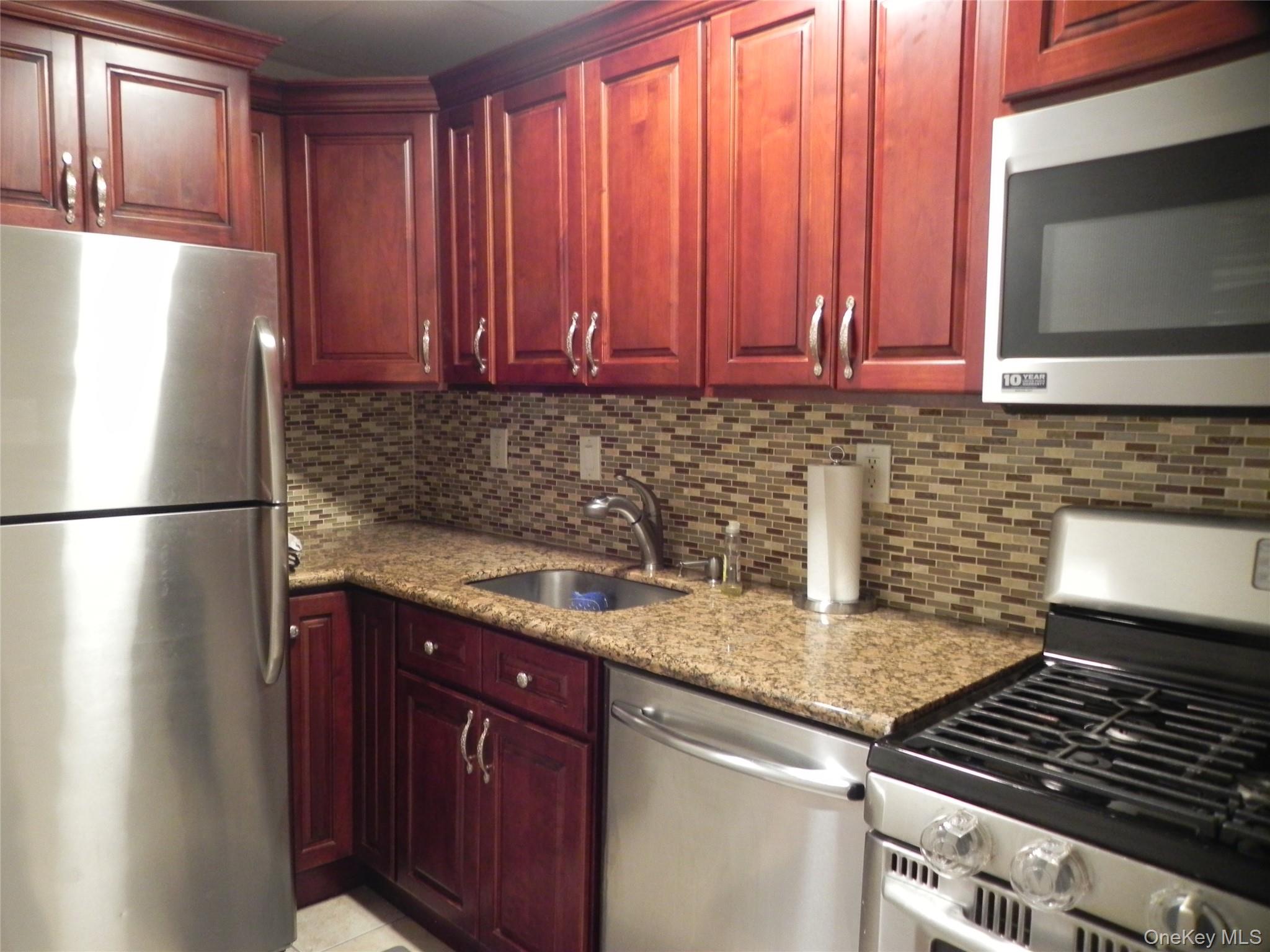 1250 North Avenue, Unit 110 New Rochelle, NY 10804 - Photo 8 of 27 Kitchen featuring appliances with stainless steel finishes, dark brown cabinets, light stone counters, and decorative backsplash
