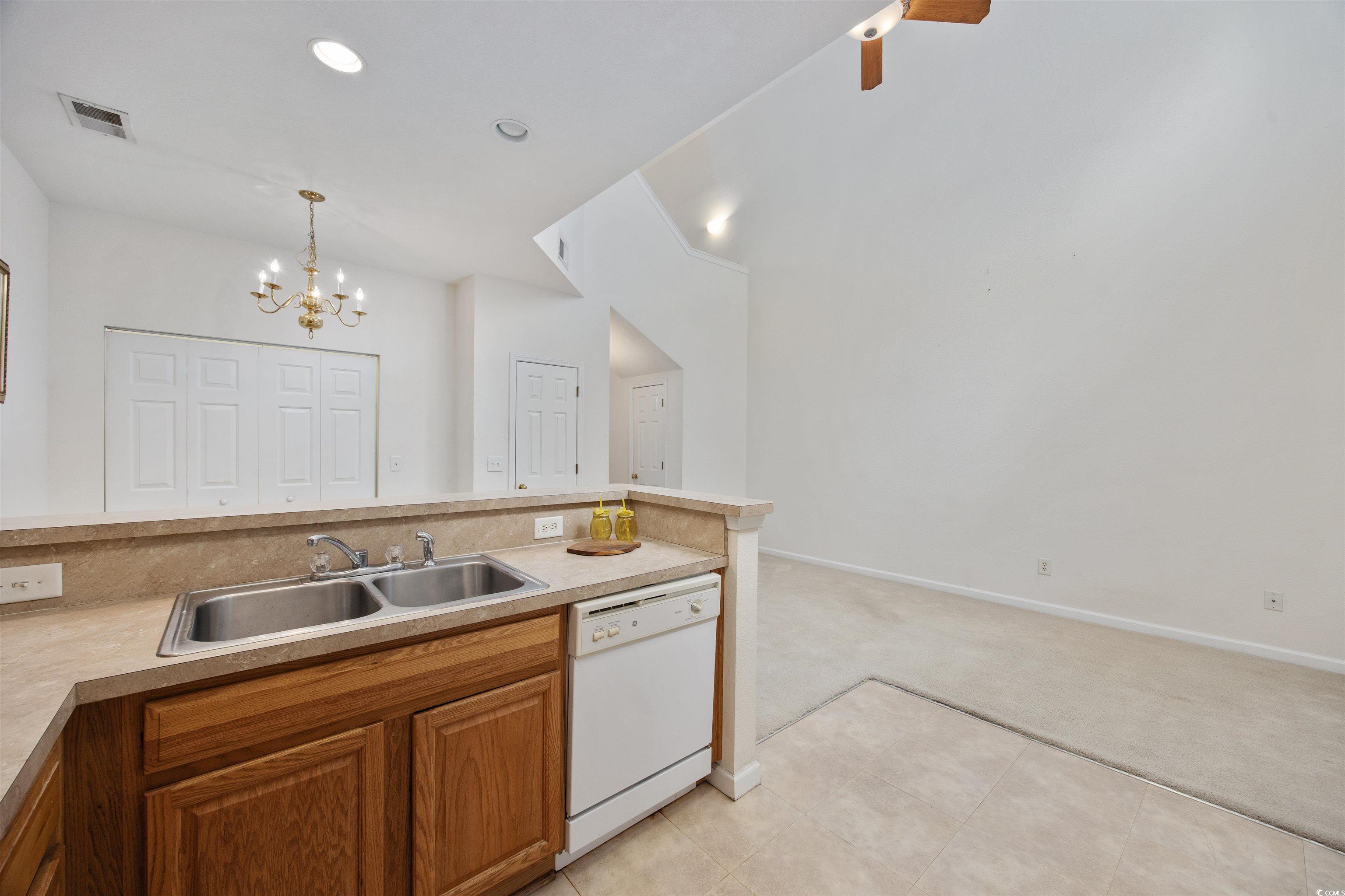 155 Chenoa Drive, Unit D Murrells Inlet, SC 29576 - Photo 9 of 33 Kitchen with white dishwasher, light colored carpet, a chandelier, brown cabinets, and decorative light fixtures
