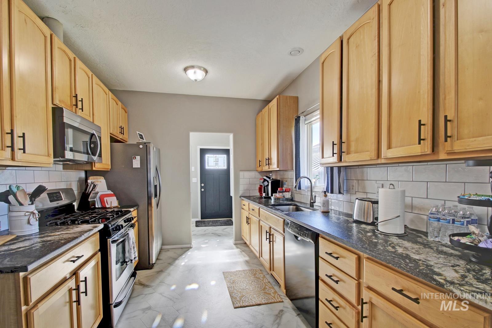 8565 South Ten Mile Road Meridian, ID 83687 - Photo 3 of 25 Kitchen featuring stainless steel appliances, decorative backsplash, light marble finish floors, light brown cabinetry, and dark stone countertops