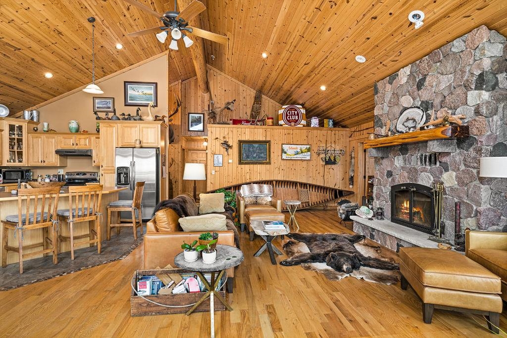 90190 Bark Point Road Herbster, WI 54844 - Photo 5 of 42 Living area featuring high vaulted ceiling, a stone fireplace, wood walls, light wood-style floors, and ceiling fan