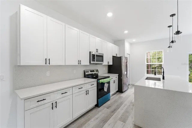 a view of a kitchen with stainless steel appliances kitchen island granite countertop a refrigerator a stove a sink and white cabinets with wooden floor