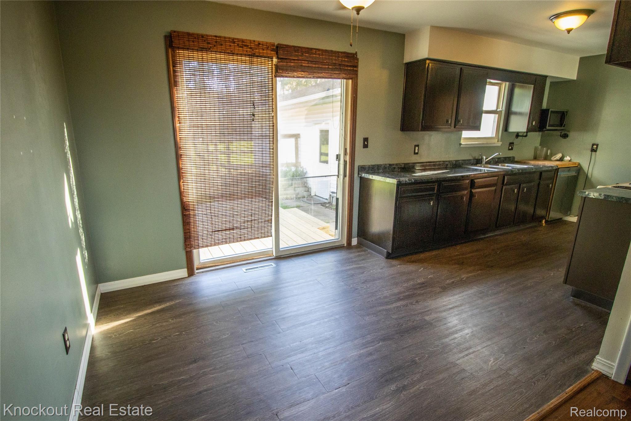 5796 East Burt Road Birch Run, MI 48415 - Photo 7 of 41 Wood-finish flooring throughout, dark-toned cabinetry, light-toned countertops, stainless steel sink, and sliding glass door to an outdoor area