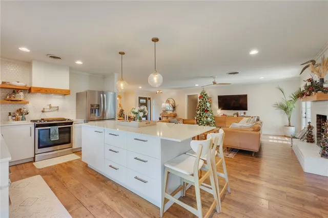 a kitchen with stainless steel appliances kitchen island granite countertop a stove top oven a sink a dining table and chairs with wooden floor
