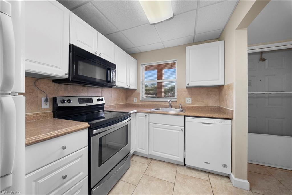170 Turtle Lake Court, Unit 109 Naples, FL 34105 - Photo 4 of 19 Kitchen featuring stainless steel range with electric cooktop, black microwave, white dishwasher, white cabinets, and a drop ceiling