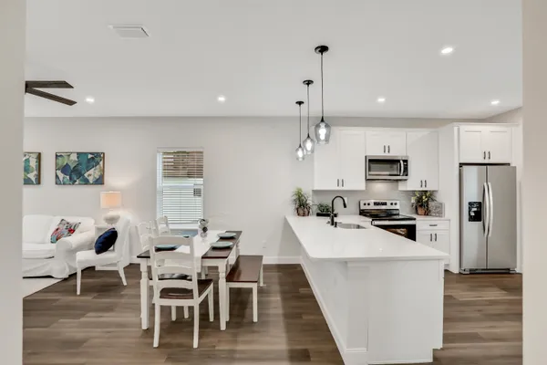a kitchen with stainless steel appliances kitchen island granite countertop a stove a refrigerator a kitchen island a dining table and chairs with wooden floor