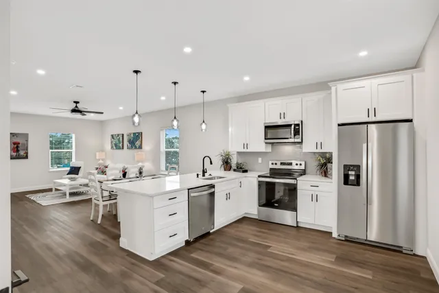 a kitchen with stainless steel appliances a stove top oven a sink a refrigerator white cabinets and wooden floor