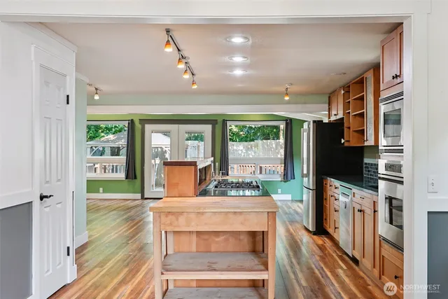 a kitchen with stainless steel appliances granite countertop a refrigerator a sink dishwasher a stove and white countertops with wooden floor