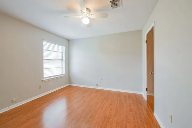 an empty room with wooden floor ceiling fan and windows