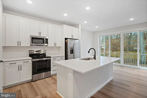 a kitchen with stainless steel appliances granite countertop a stove a sink a refrigerator and white cabinets with wooden floor