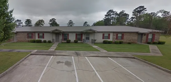 a view of a white house next to a yard with big trees