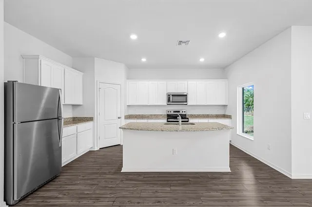 a kitchen with stainless steel appliances granite countertop a refrigerator a stove a sink and white cabinets with wooden floor