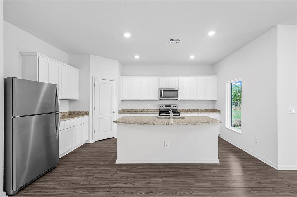 7886 99th Court Vero Beach, FL 32967 - Photo 6 of 18 a kitchen with stainless steel appliances granite countertop a refrigerator a stove a sink and white cabinets with wooden floor
