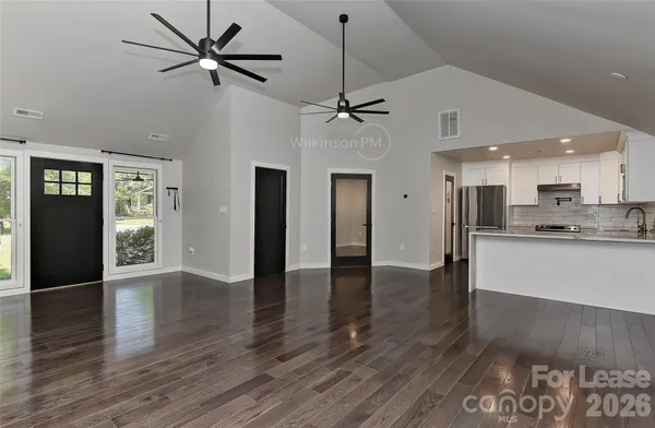a view of an empty room with wooden floor and a kitchen