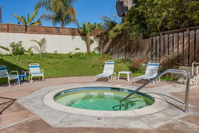 a small pool with lawn chairs and wooden fence