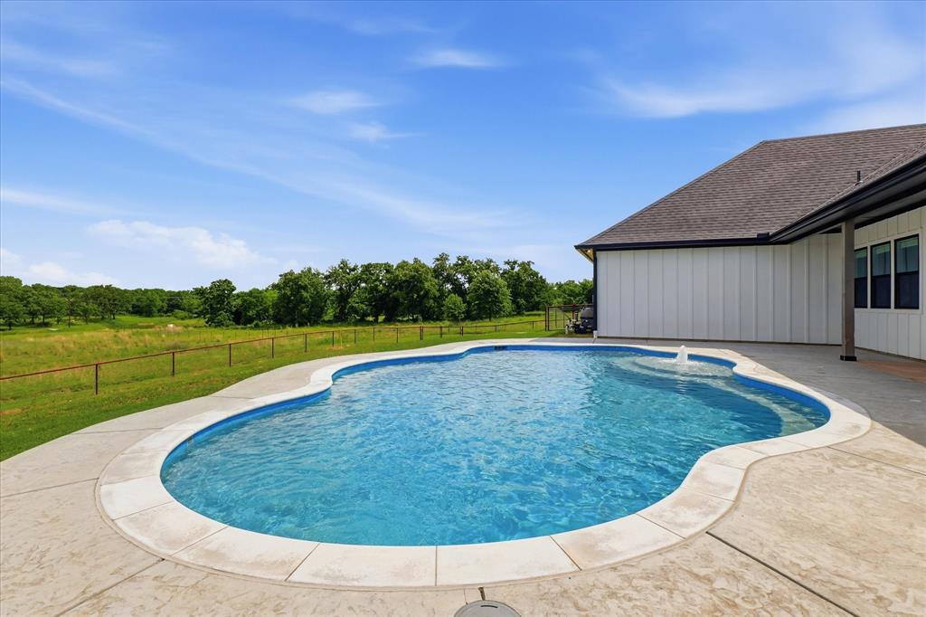 120 Grace Vw Road Weatherford, TX 76088 - Photo 35 of 40 Curved inground pool with integrated fountain and concrete decking, bordered by a white board-and-batten exterior and a covered patio