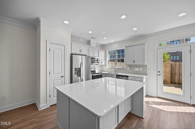 a kitchen with kitchen island wooden floors white cabinets and stainless steel appliances