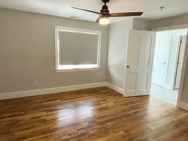 an empty room with wooden floor fan and windows