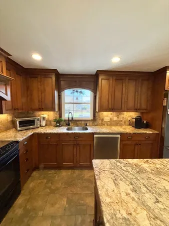 a large kitchen with granite countertop a stove top oven a sink dishwasher and wooden cabinets