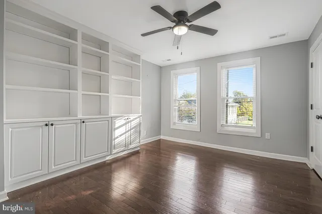 an empty room with wooden floor chandelier fan and windows