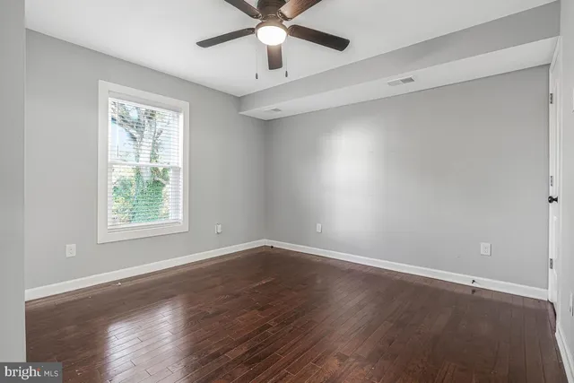 an empty room with wooden floor fan and windows