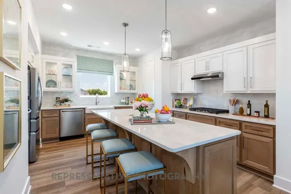 a kitchen with stainless steel appliances a stove a sink a refrigerator white cabinets and wooden floor