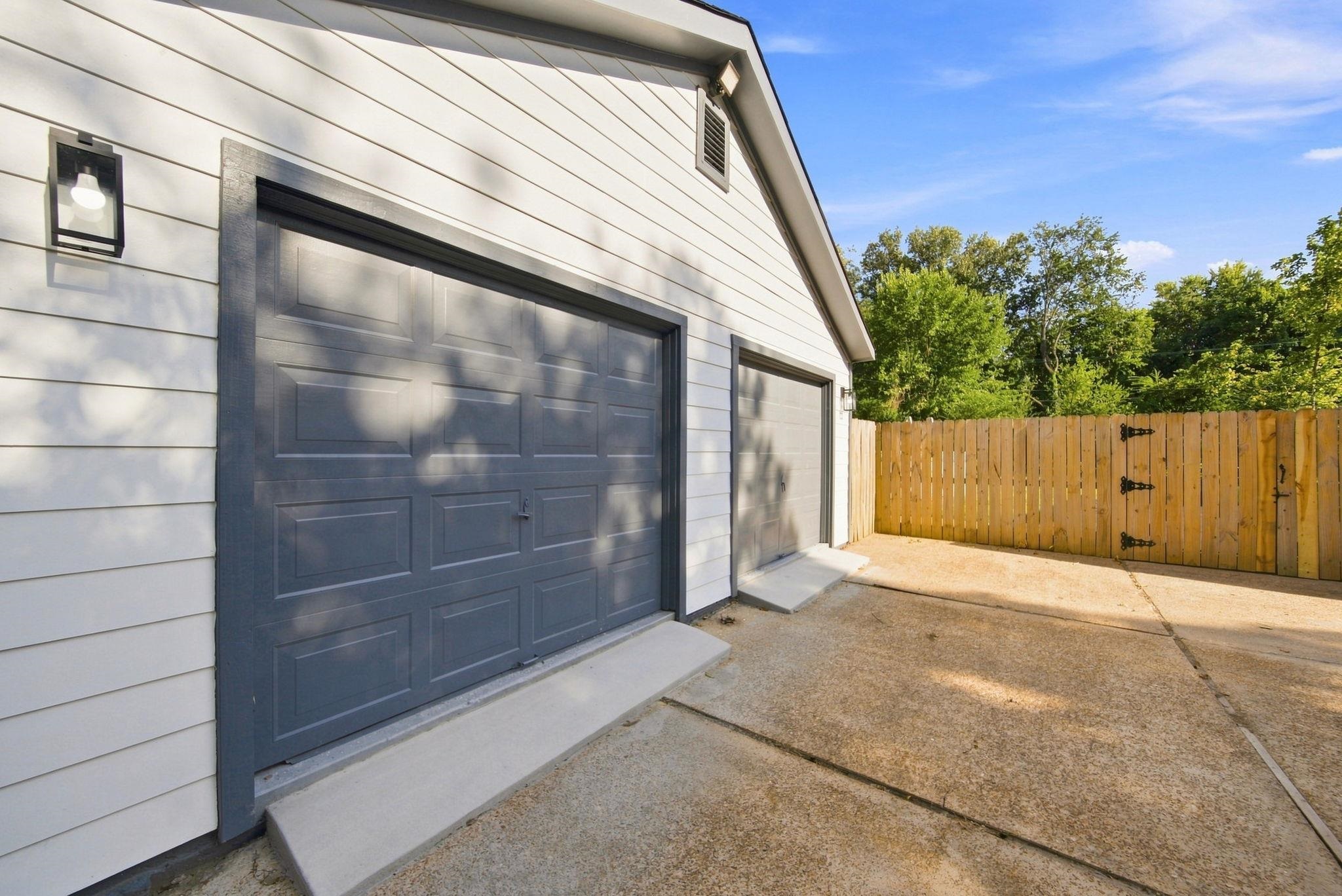 458 Gerald Road Memphis, TN 38122 - Photo 4 of 37 Two gray garage doors, white horizontal siding, black exterior light fixture, and a wood privacy fence