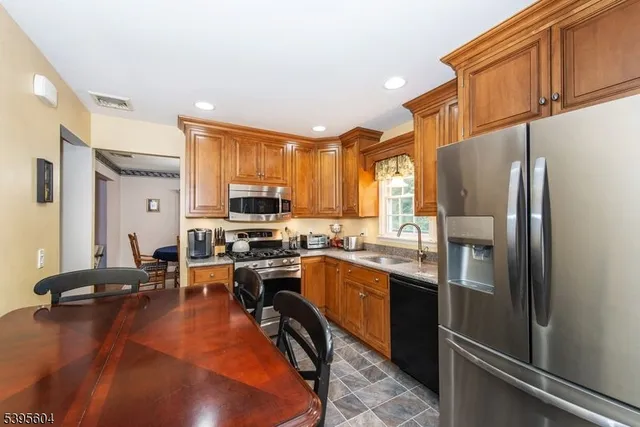 a kitchen with stainless steel appliances granite countertop a refrigerator a stove a sink dishwasher a dining table and chairs with wooden floor