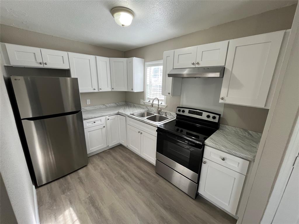 7642 Maxwell Avenue Dallas, TX 75217 - Photo 7 of 20 Kitchen featuring appliances with stainless steel finishes, white cabinetry, a textured ceiling, light wood-style flooring, and under cabinet range hood