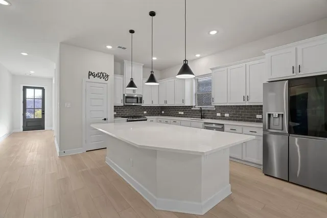 a large kitchen with stainless steel appliances kitchen island granite countertop a stove a refrigerator a sink and a oven with white cabinets