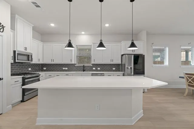 a large kitchen with stainless steel appliances kitchen island a stove a sink a center island and a wooden floor