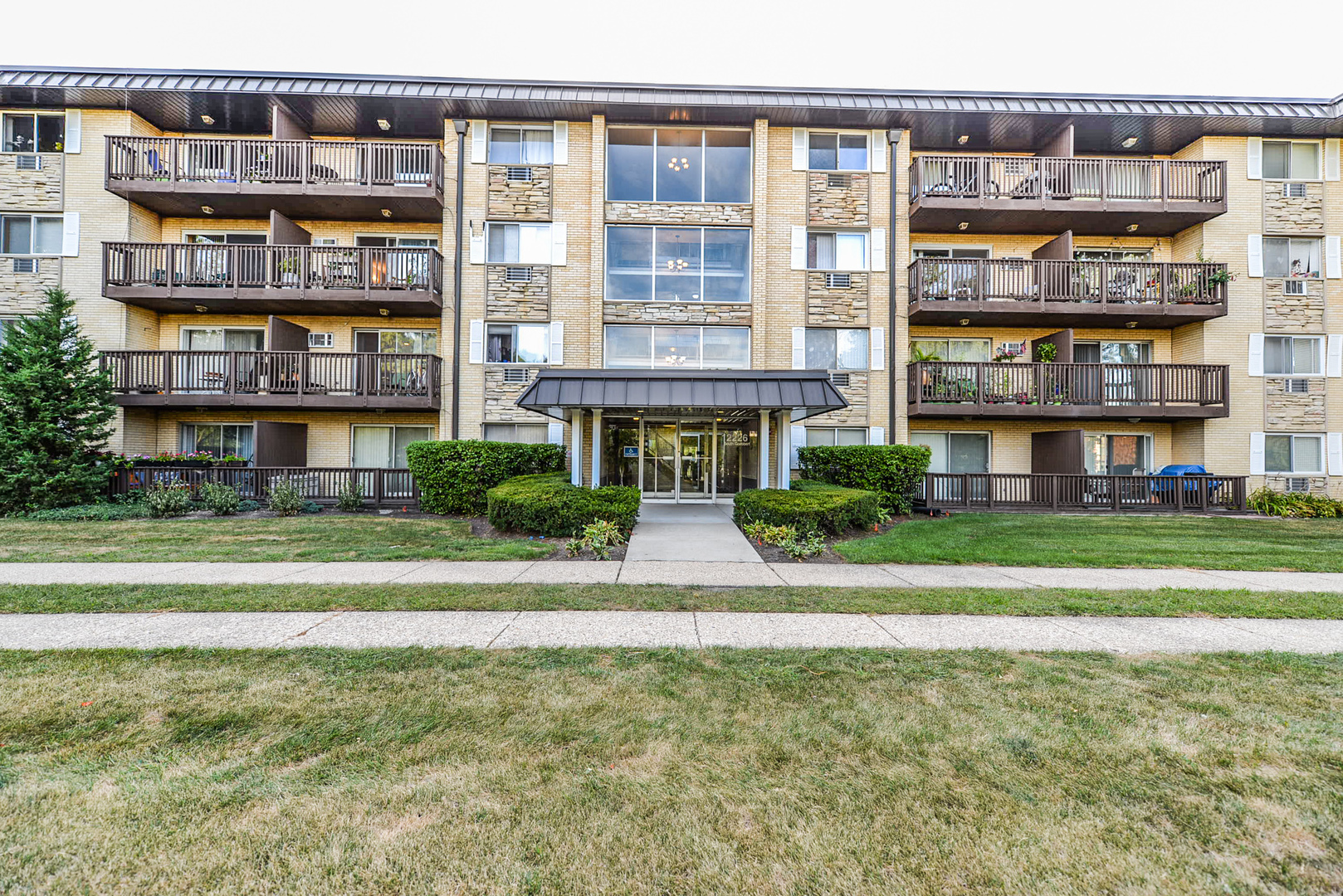 a front view of multi story residential apartment building with a yard and large trees